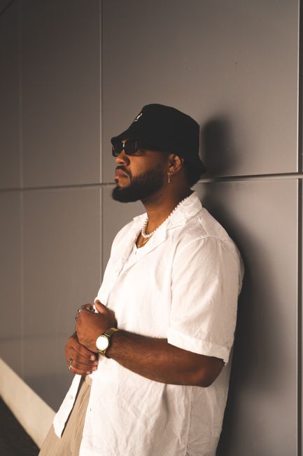 Fashionable man with beard and sunglasses in modern streetwear leaning against a wall, exuding urban style.