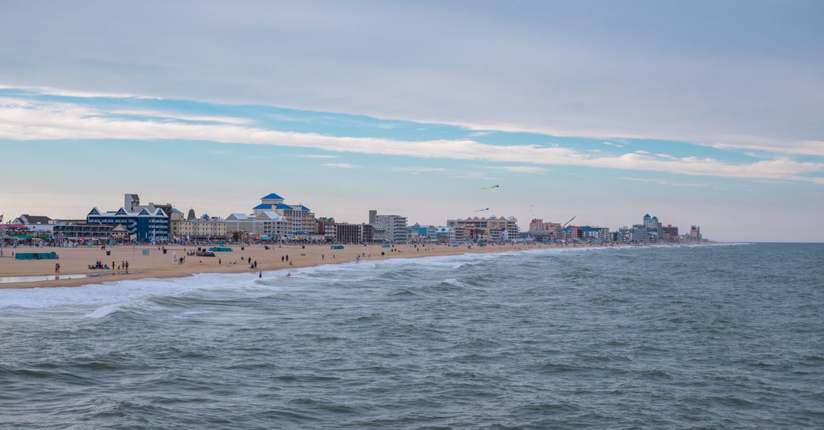 Peaceful beach scene with city buildings and a vast ocean under a serene sky.