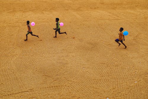 Kids Holding a Balloon while Running on Brown Sand
