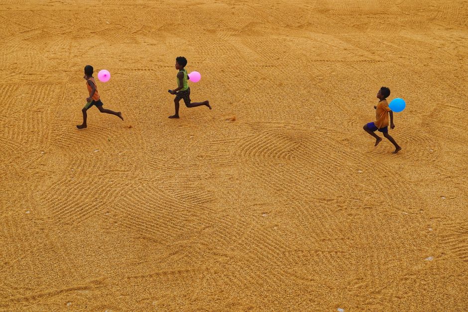 Children playing with balloons on a sandy surface in Habra, India, capturing youthful joy.