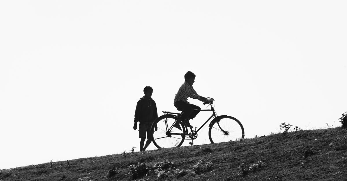 Silhouette of children riding a bicycle on a hill in Purulia, India, under a clear sky.