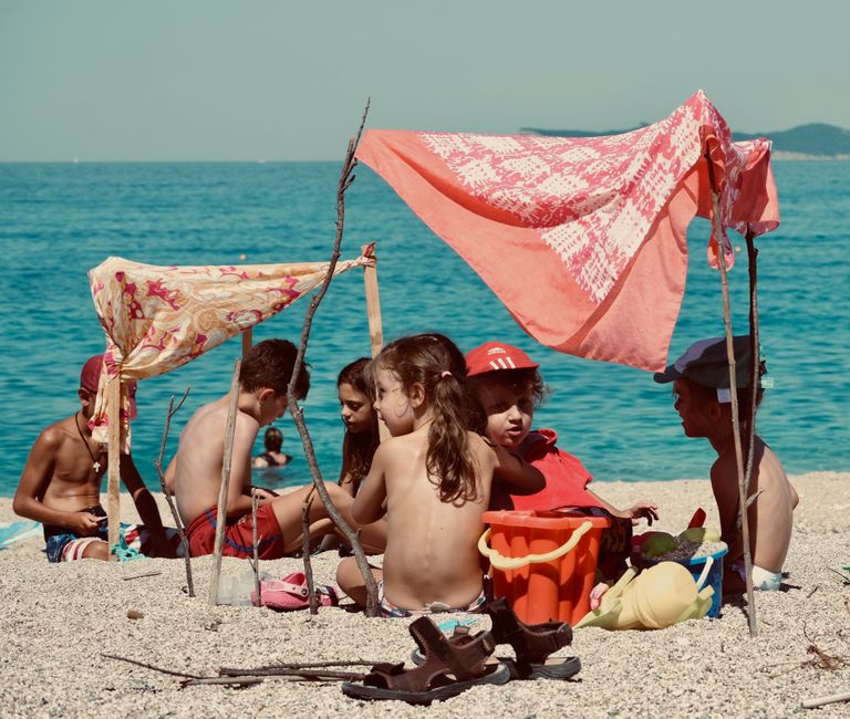 Children enjoying a sunny summer day on the beach in Perdika, Greece, building a beach shelter.