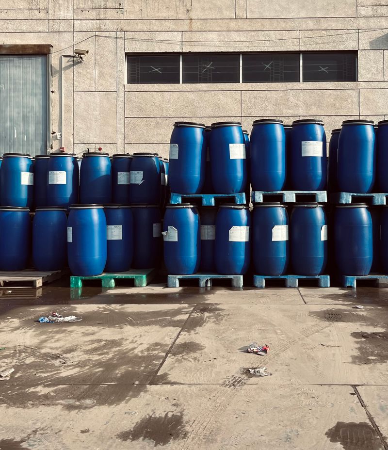 Rows of blue industrial chemical barrels stacked on pallets outside a warehouse for sulfuric acid storage
