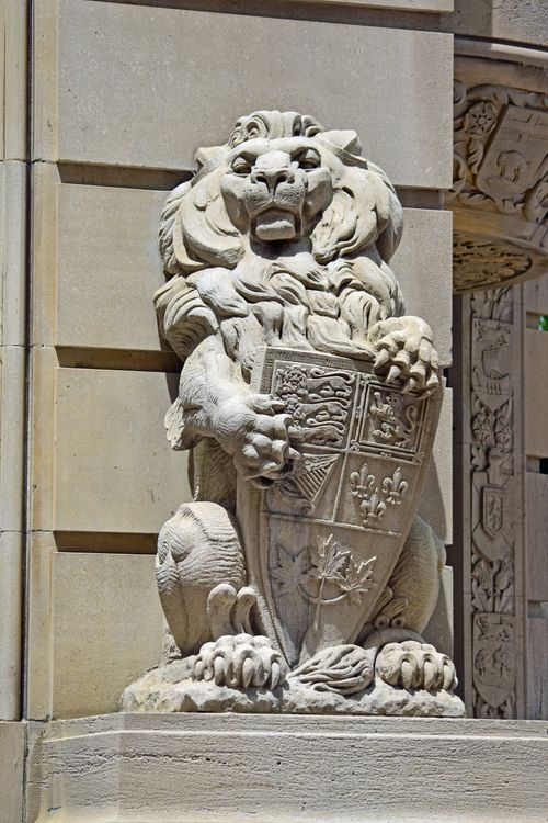 Free Detailed stone lion sculpture holding an intricate shield on a building facade. Stock Photo
