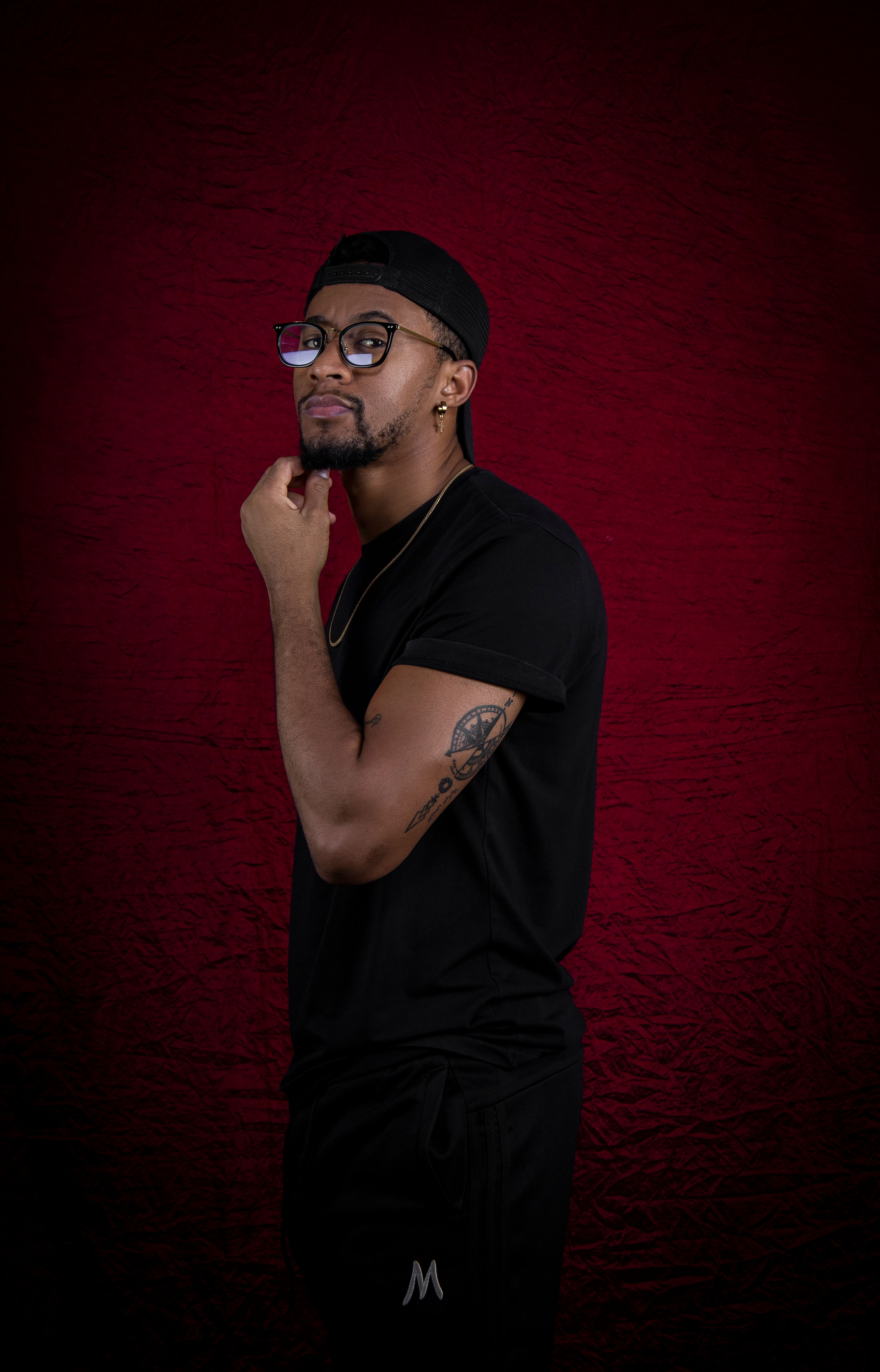 Portrait of a stylish man wearing glasses and a black outfit against a rich red background.