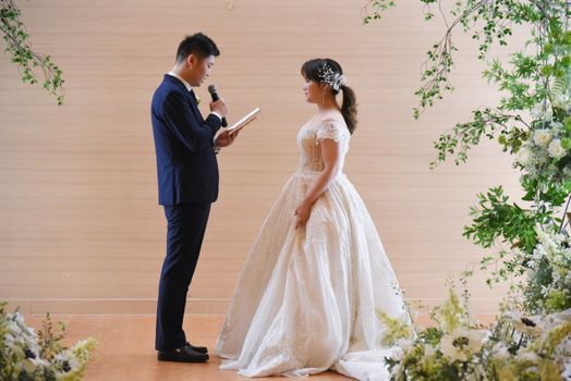 A bride and groom share vows in an elegant indoor ceremony with floral decorations.