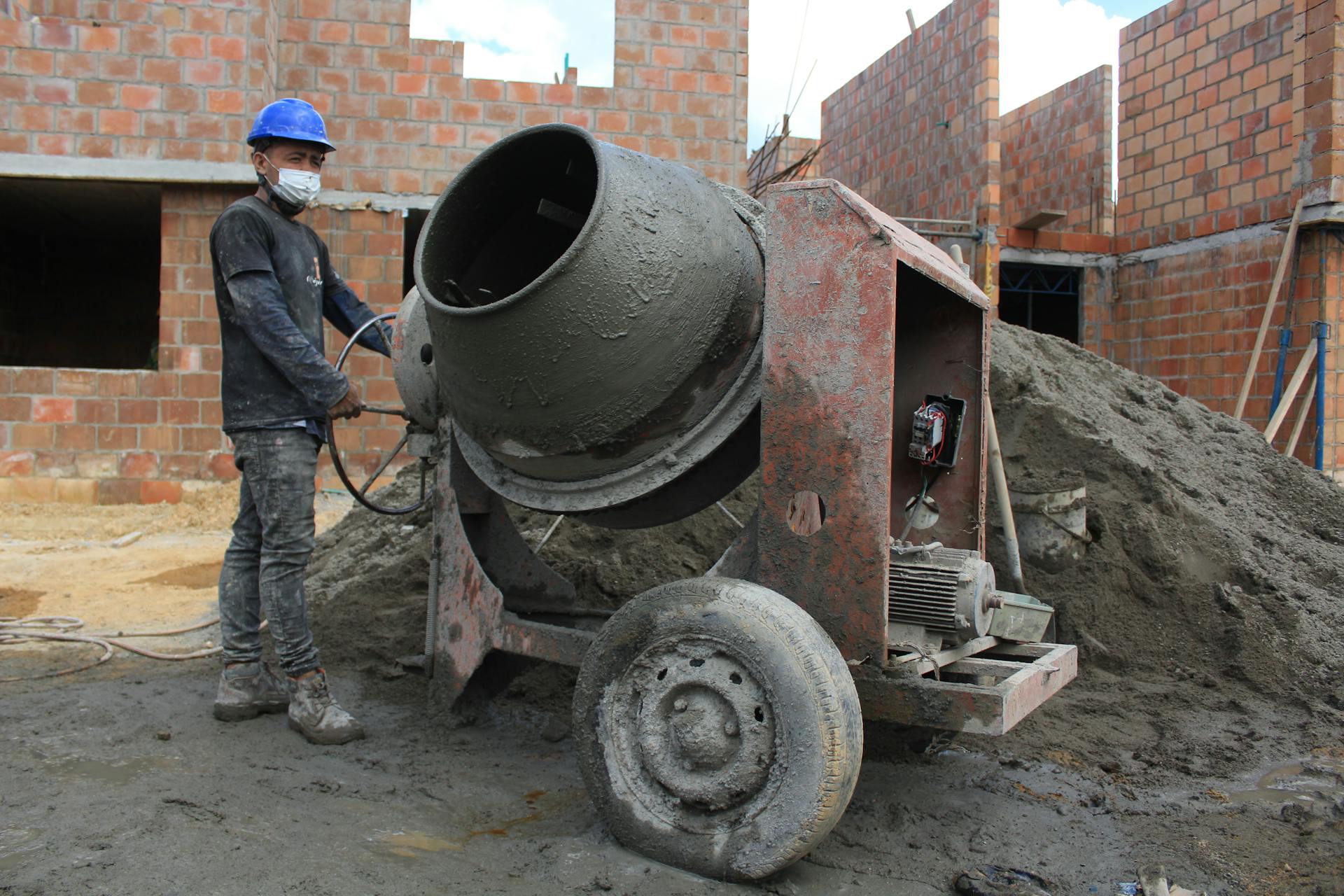 A construction worker in safety gear operates a cement mixer at a building site.