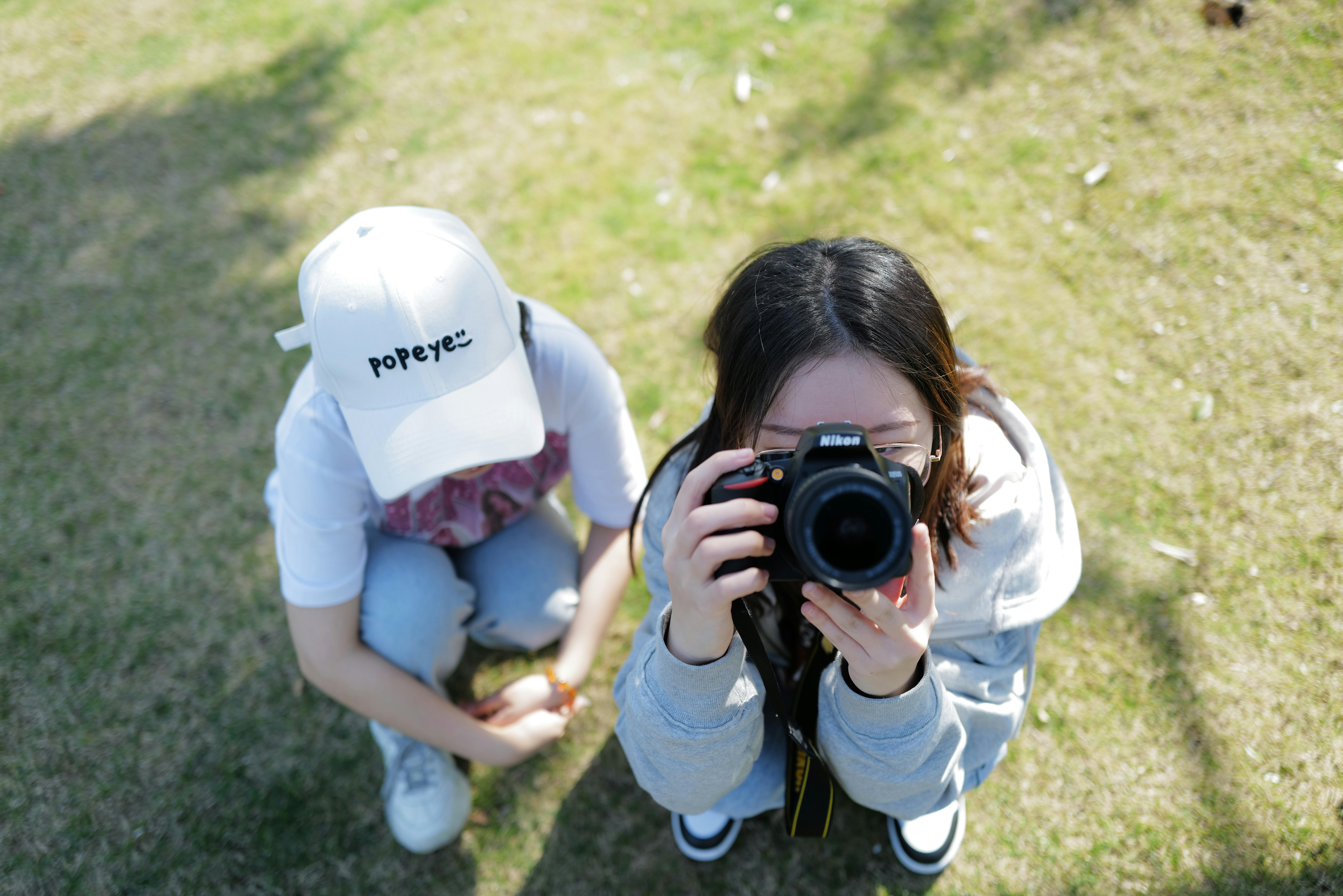 High-angle view of two girls taking photos with a Nikon camera outdoors.
