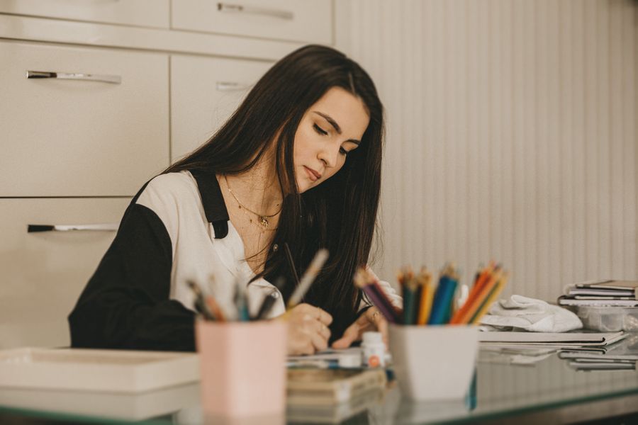 Caucasian woman writing in office using colored pencils, surrounded by stationary supplies.