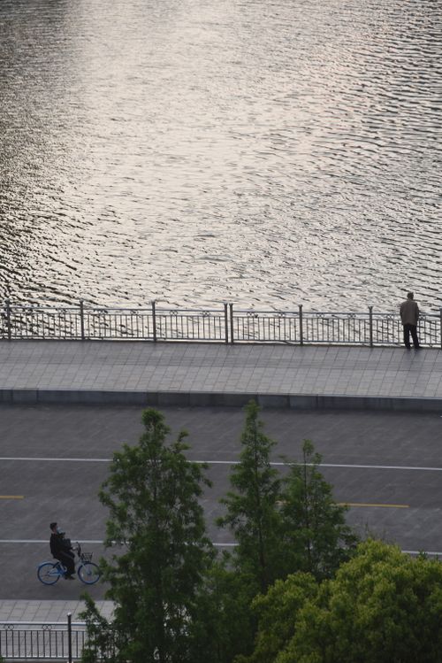 Free A serene riverfront scene featuring a bicyclist and a solitary walker, captured from above. Stock Photo