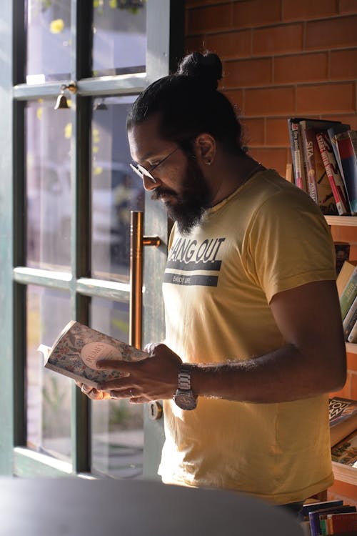 Bearded Man in Yellow Shirt Reading a Book on Doorway
