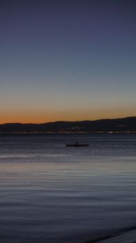 A tranquil scene of a silhouetted boat at twilight, reflecting serene colors over calm waters.