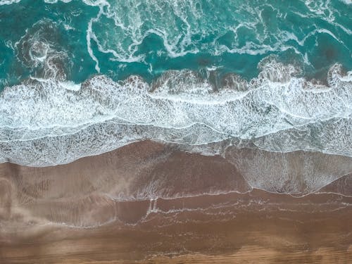 Aerial Shot of Turquoise Surf Waves and Foam Splashing on a Sandy Beach