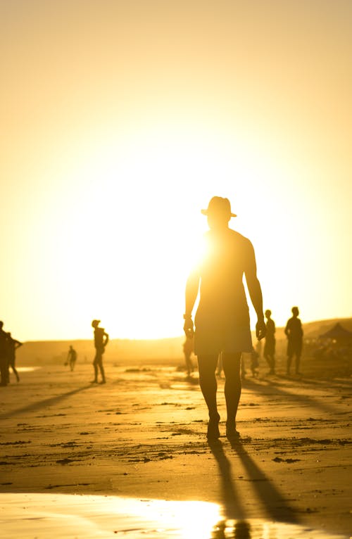 Silhouette of a Man in a Hat Walking on the Beach 