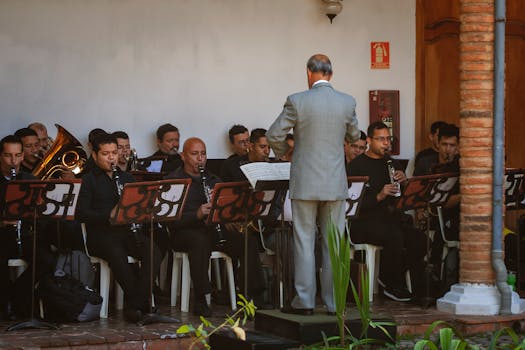 Orchestra musicians playing wind instruments indoors led by conductor.