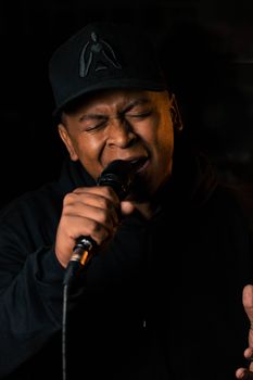 Close-up of an African American male singer passionately performing on a dark stage.