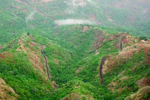 A scenic aerial view showcasing a winding road traversing lush green mountains under misty skies.