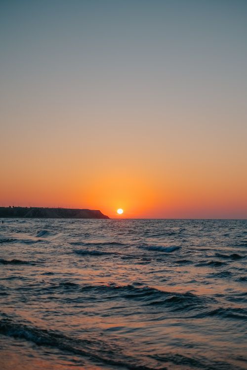 Free Serene ocean sunset with vibrant orange sky and rippling waves. Stock Photo