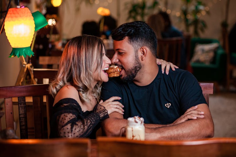 Couple Sitting On Wooden Chair Biting Cupcake