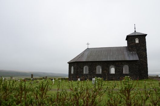 Stone church in Iceland with a lush grass field and a white, cloudy sky.
