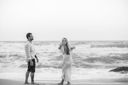 Grayscale Photo of Man and Woman Standing on Beach 