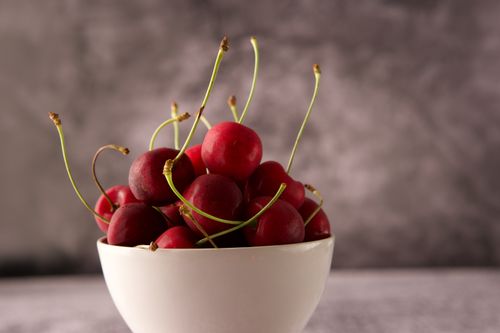Free A ceramic bowl brimming with vibrant red cherries, showcased against a blurred background. Stock Photo