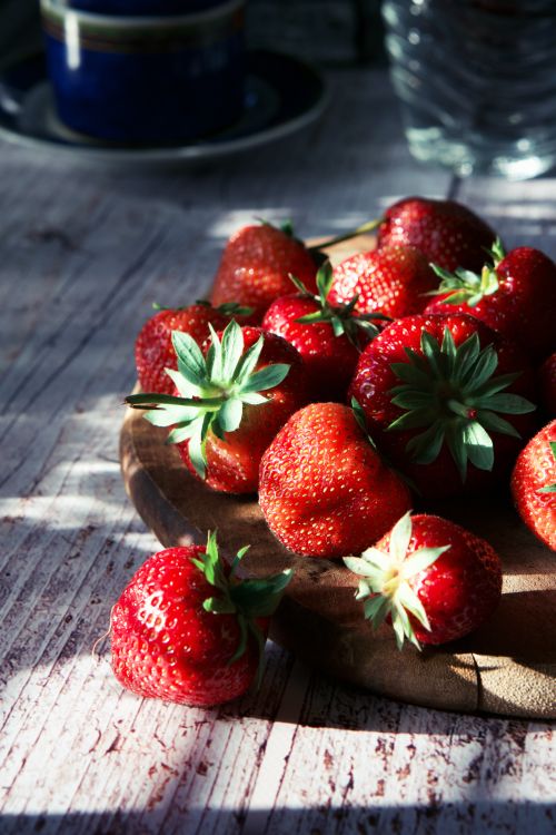 Free Close-up of ripe red strawberries on a wooden board with rustic texture in sunlight. Stock Photo