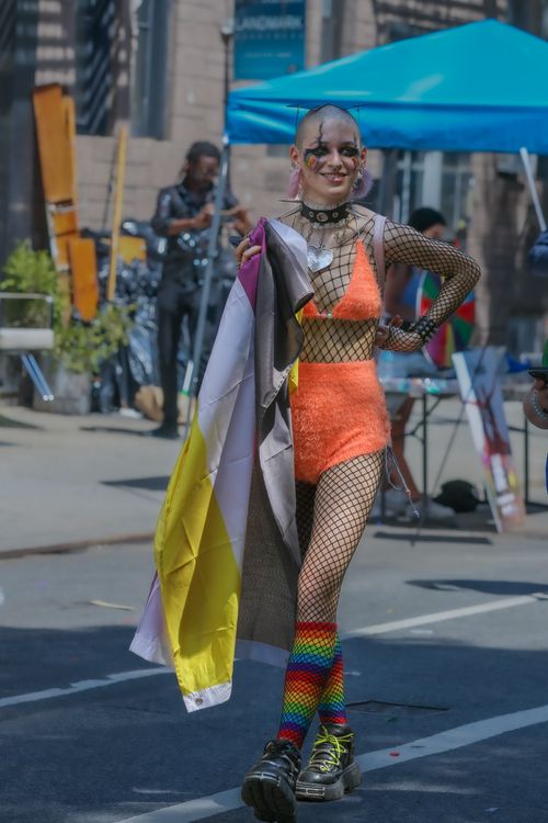 Free Person celebrating Pride with colorful outfit and flag outdoors in a city setting. Stock Photo