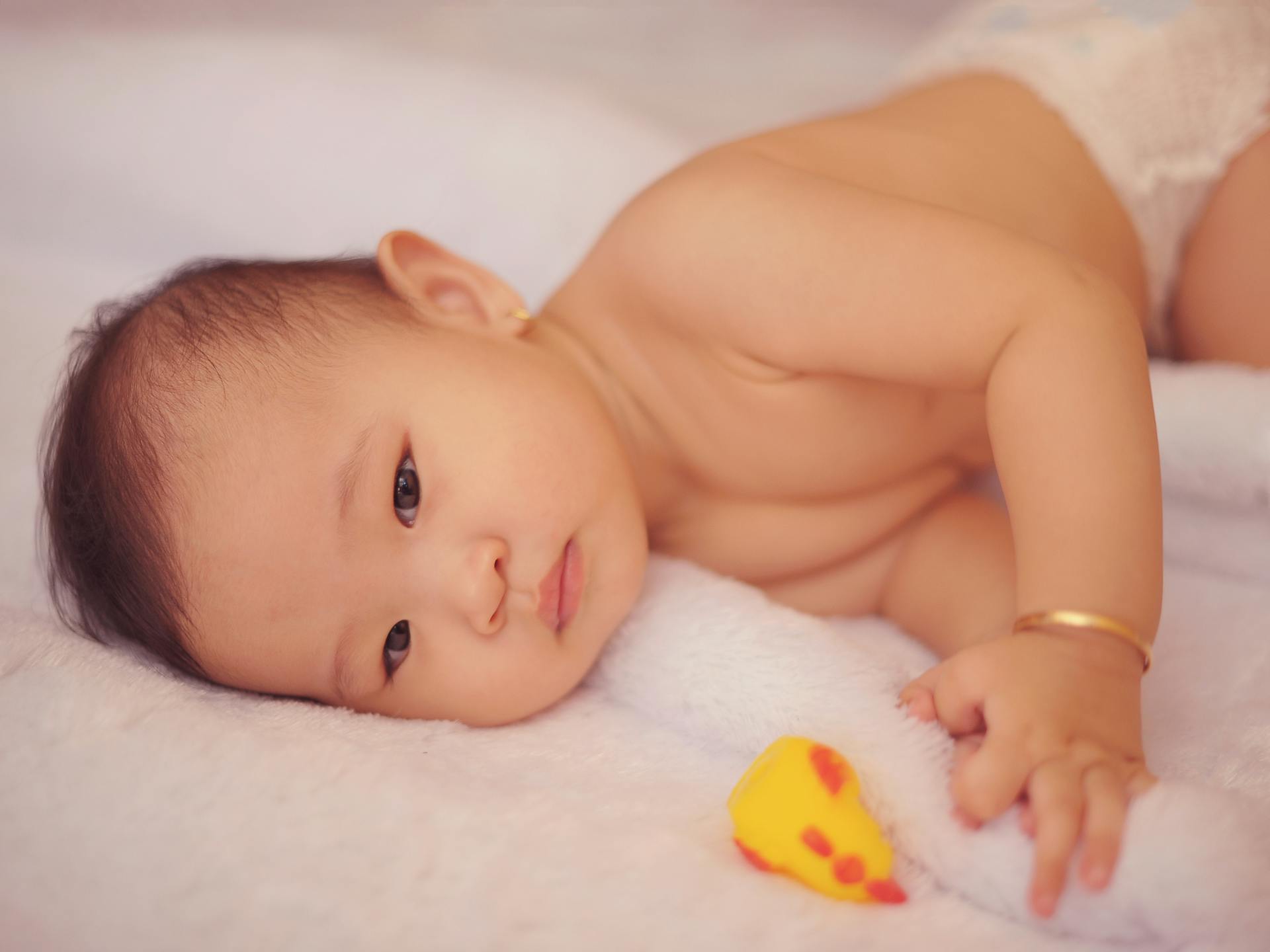 Close-up of a cute newborn baby wearing a diaper and bracelet, resting indoors.