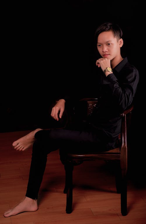Man Wearing All Black Outfit Sitting on a Wooden Chair 
