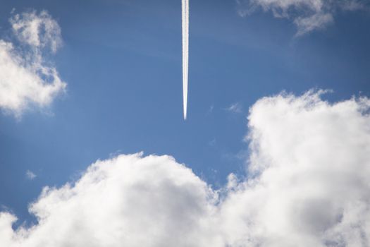 Jet airplane contrail streaking through fluffy white clouds in blue sky.