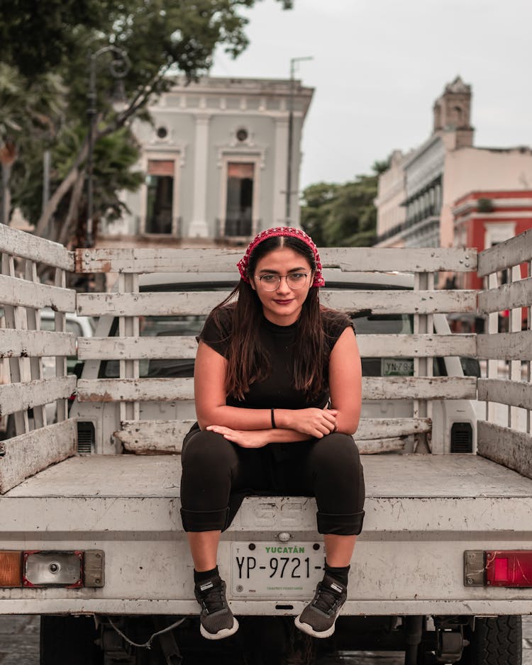 A Woman In Black Shirt And Pants Sitting At The Back Of A Truck