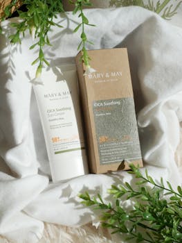 Close-up of Mary & May CICA Soothing Sun Cream on soft fabric with greenery.