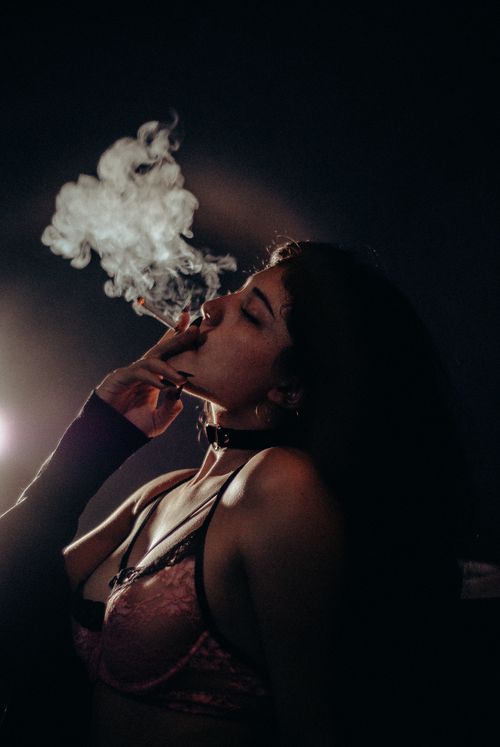 Free Artistic portrait of a woman smoking, backlit with moody lighting and a seductive pose. Stock Photo
