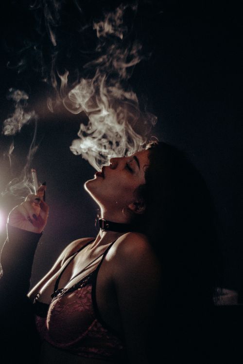 Free Moody side profile of a woman exhaling smoke in dim lighting, showcasing her elegance. Stock Photo
