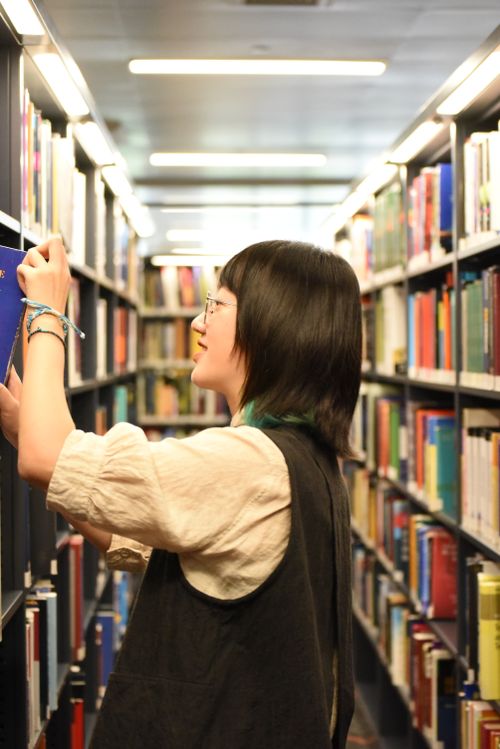 Free Side view of a young student browsing books in a library aisle. Stock Photo