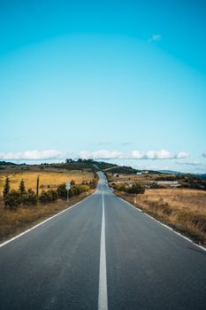 Empty asphalt road stretching through serene countryside with blue sky backdrop.