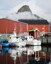 Picturesque boats docked in Reine, Lofoten, with reflections and misty mountains.