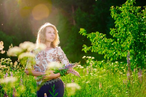 Free A woman enjoys the sunshine in a lush flower field, holding wildflowers. Stock Photo