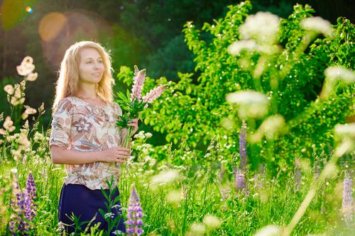 Free A woman with blond hair poses in a lupine flower field on a sunny day, conveying a sense of tranquility. Stock Photo