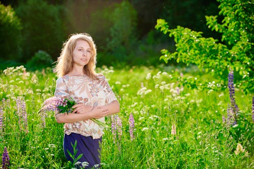 Woman in Floral Blouse Holding Flowers while Standing on Flower Field