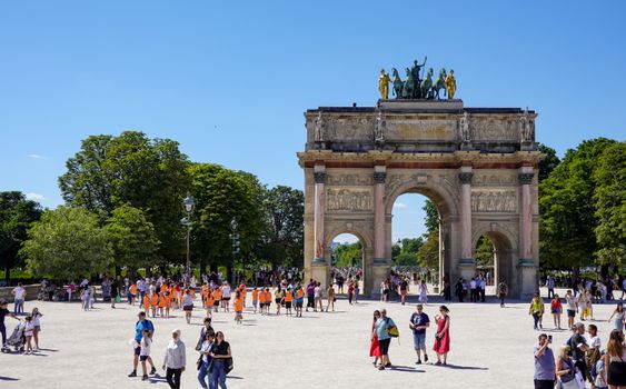 Lively summer day at the Arc de Triomphe du Carrousel in Paris with tourists and lush greenery.