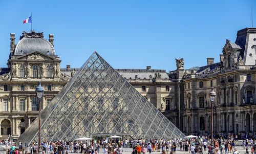 Free Iconic glass pyramid of Louvre Museum surrounded by tourists on a sunny day in Paris. Stock Photo