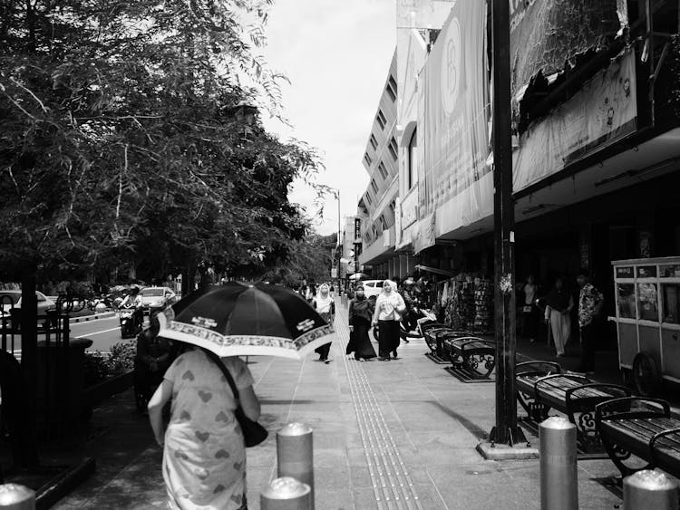 Grayscale Photo Of Person Holding Umbrella Walking On Sidewalk