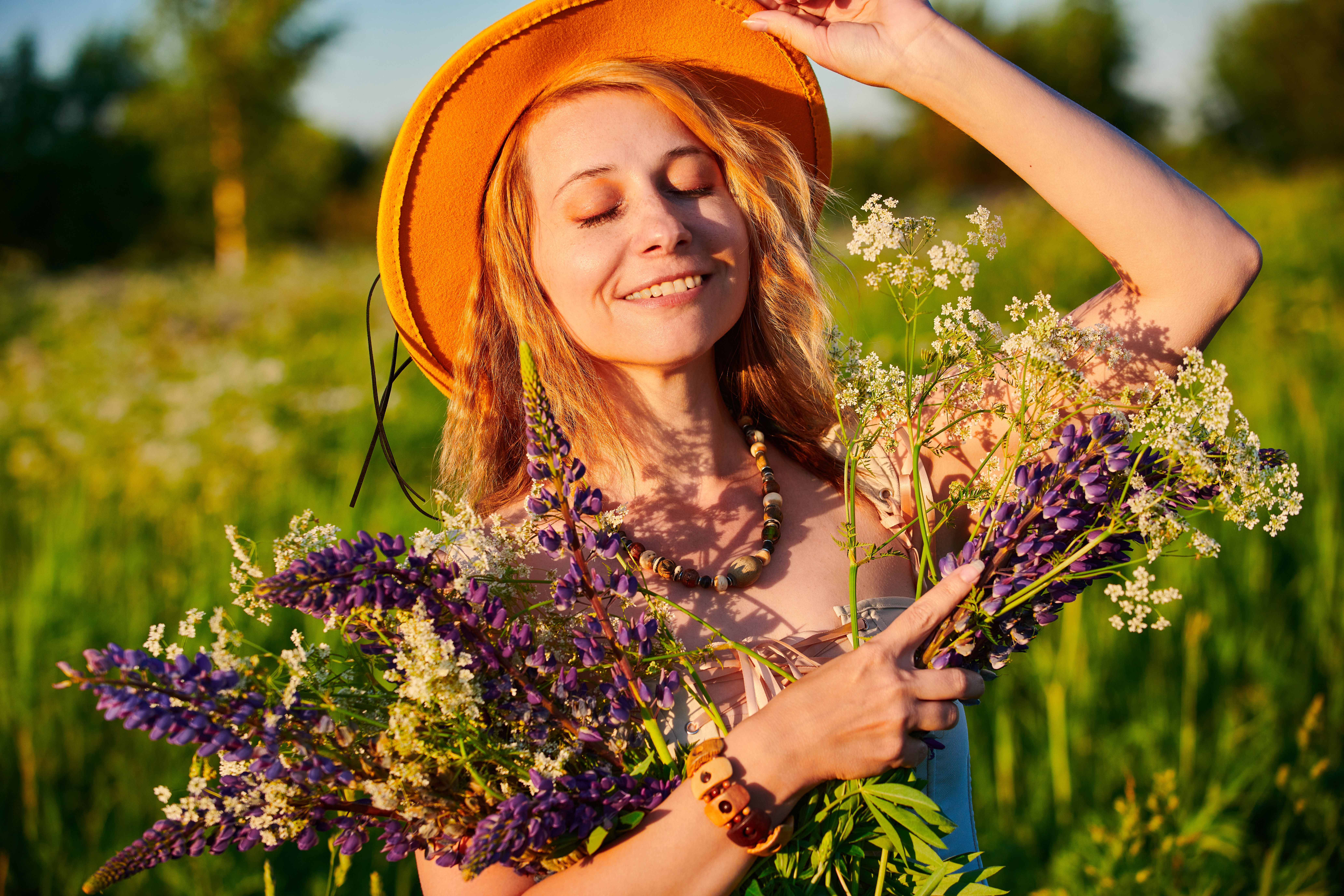 Smiling woman in a yellow hat holding a vibrant bouquet in a sunny field.