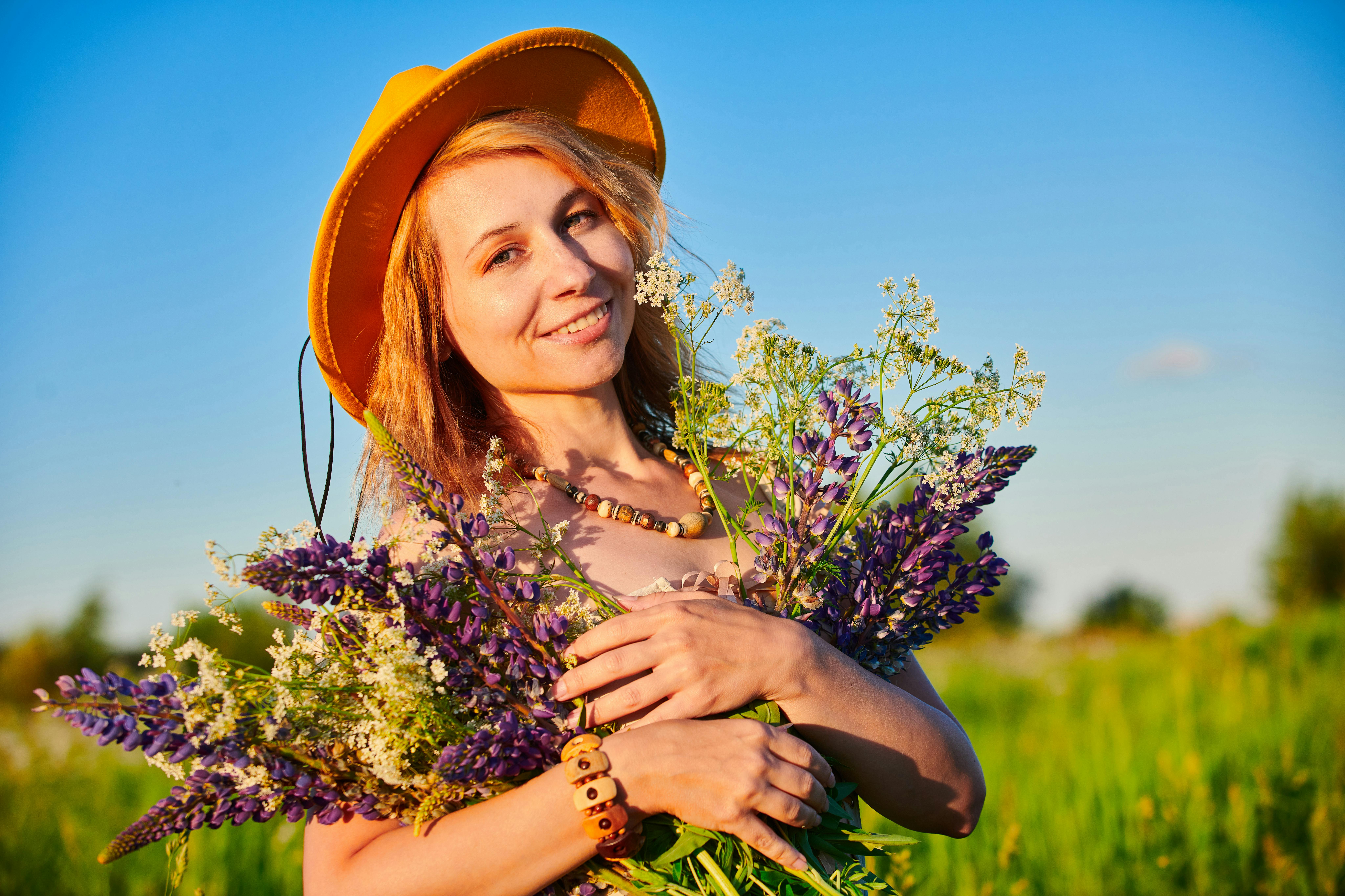 A joyful woman in a yellow hat embraces a vibrant bouquet of wildflowers in a sunlit field.