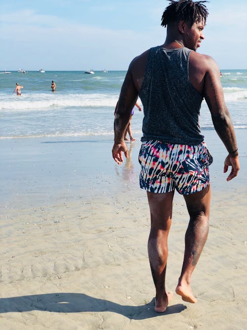 Man Wearing Grey Tank Top Walking On Seashore