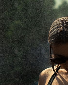 Close-up of a woman wearing sunglasses during a rain shower, with a dramatic and moody ambiance.