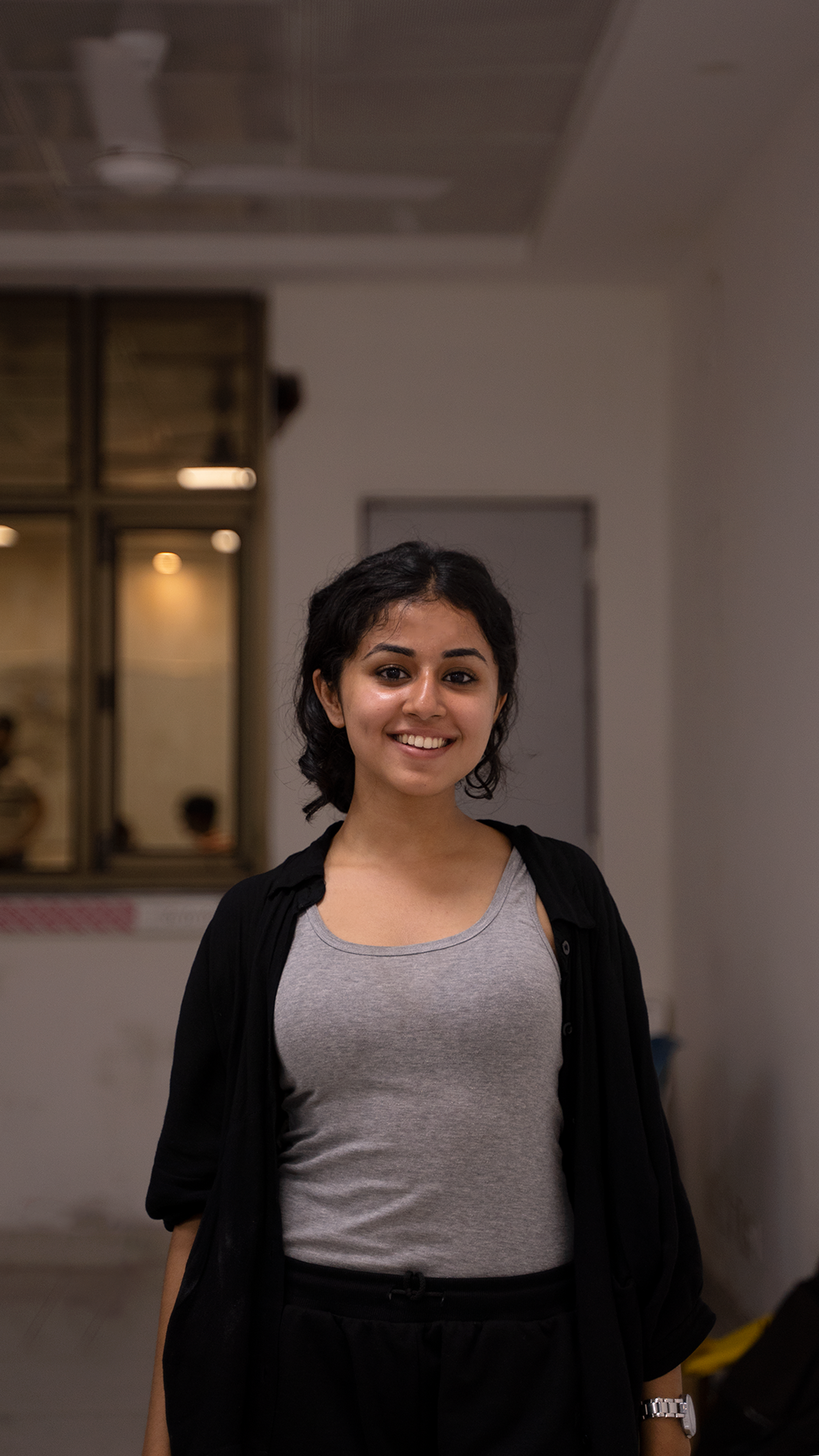 Portrait of a smiling young woman in a black cardigan and gray tank top indoors.