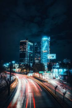 A stunning night view of Mexico City's modern skyscrapers with light trails in the foreground, capturing urban vibrancy.